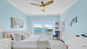 A bedroom with a bed, a ceiling fan, a window with a view of the water, and a chair. - Lagoon Front | Pet Friendly | Deeded Beach Access, Pool & Pier (Gulf Shores)