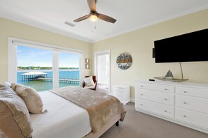 A bedroom with a bed, a ceiling fan, a TV, a dresser, and a view of the water. - Lagoon Front | Pet Friendly | Deeded Beach Access, Pool & Pier (Gulf Shores)
