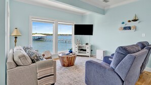A living room with a view of the water, a sofa, a chair, a coffee table, and a flat-screen TV. - Lagoon Front | Pet Friendly | Deeded Beach Access, Pool & Pier (Gulf Shores)
