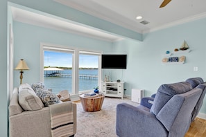 A living room with a view of the water, a flat-screen TV, a sofa, and a coffee table.