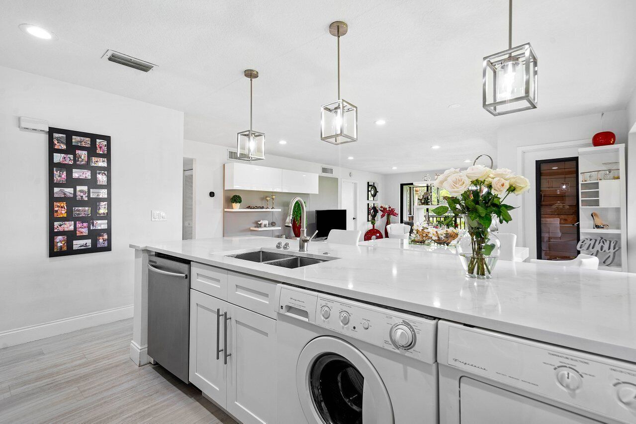 A modern kitchen with a built-in washer and dryer, a large island with a sink, pendant lights, and a wall-mounted photo collage.