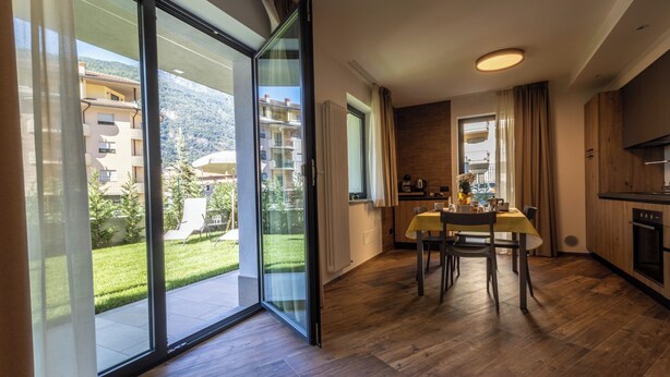 A modern kitchen with a dining area, large sliding glass doors to a balcony, and a view of a residential area. - Three-room apartment with garden (Pont-Saint-Martin)