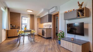 A modern kitchen with wooden cabinets, a dining area with a table and chairs, and a built-in TV on a wooden console. - Three-room apartment with garden (Pont-Saint-Martin)