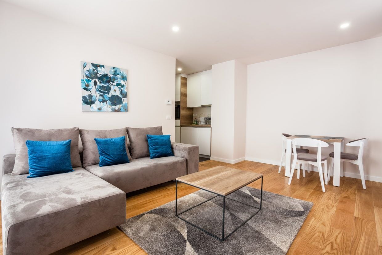 A modern living room with a grey sectional sofa, a wooden coffee table, and a dining area with white chairs and a table.