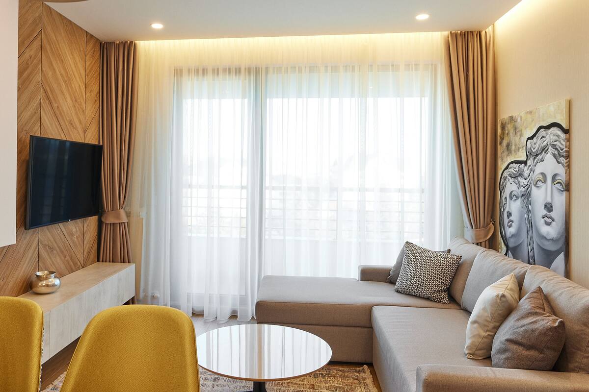 Ein modernes Wohnzimmer mit einer Couch, zwei gelben Sessel, einem Couchtisch und einem Flachbildfernseher, der an einer Holzpaneelwand befestigt ist.