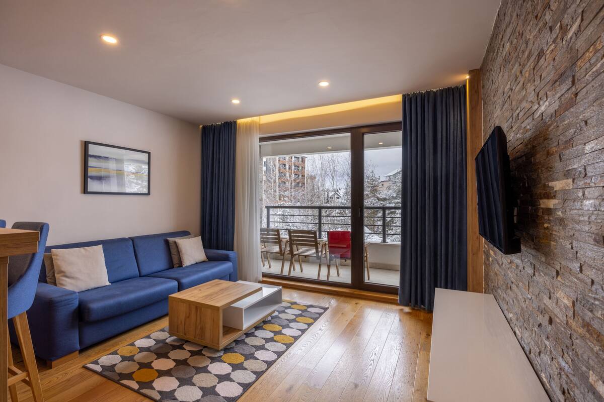 Ein modernes Wohnzimmer mit einem blauen Sofa, einem Holztisch und einem gemusterten Teppich.