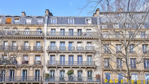 A multi-story building with balconies, windows, and a sign reading "PAPETERIE".