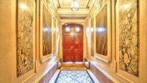 A hallway with a marble floor, a red door with a brass handle, and a light fixture on the ceiling.