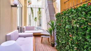 A narrow outdoor balcony with a white sofa, a small table, and a potted plant.