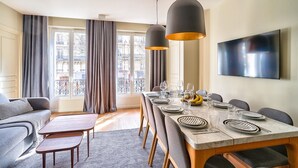 A dining area with a long table set for six, a sofa, and a TV mounted on the wall.