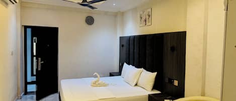 A hotel room with a bed, a round table, a chair, a ceiling fan, and a clock on the wall.