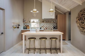 Een keuken met een centraal eiland, barstoelen, hangende吊り灯 en houten kastjes.