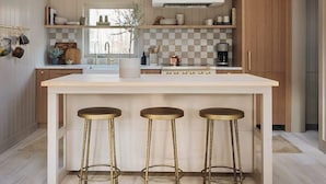 Una cocina moderna con techo de madera, luces colgantes, una isla central con taburetes y vistas al exterior.