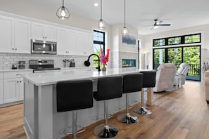 A modern kitchen with white cabinetry, a central island with bar stools, a microwave, and a stove.