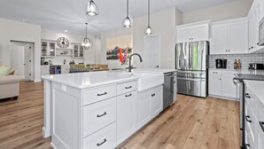 Una cucina moderna con mobili bianchi, elettrodomestici in acciaio inossidabile e illuminazione a sospensione.