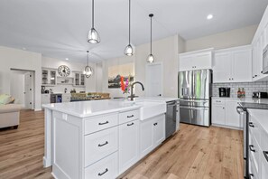 Une cuisine moderne avec des meubles blancs, des appareils en acier inoxydable et des luminaires suspendus.