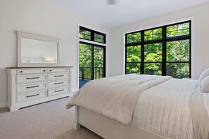 Un dormitorio con cama, cómoda y ventanas amplias con vista a árboles.