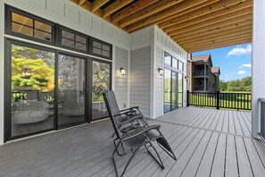 Une terrasse couverte avec une chaise, de grandes portes-fenêtres coulissantes et une vue sur une maison.
