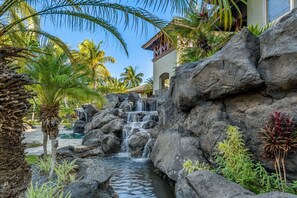 A tropical resort with a waterfall, palm trees, and a pool. - Mauna Lani Fairways 603: Luxe 2BR Home w/ Modern Comforts, Jacuzzi & Lanai Views (Kamuela)