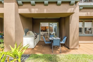 An outdoor patio with a dining table and chairs, a grill, and a view into the house.