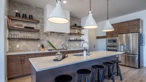 Een moderne keuken met een centraal eiland, barstoelen, roestvrijstalen apparatuur en hanglampen.