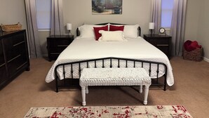 Een slaapkamer met een bed, nachtkastjes, een bankje, een dressoir en een vloerkleed.