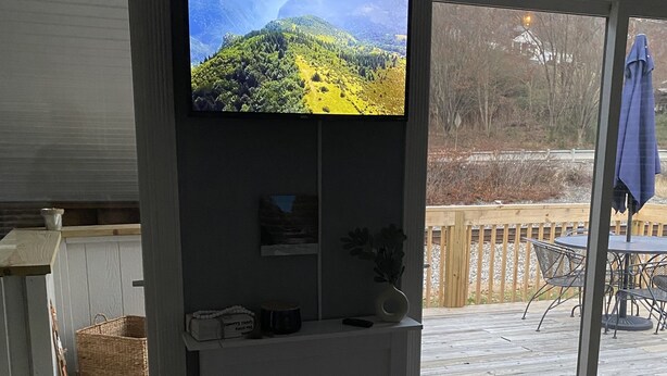 Een woonkamer met een open haard, een aan de muur bevestigde televisie, en uitzicht op een terras en buitenruimte.