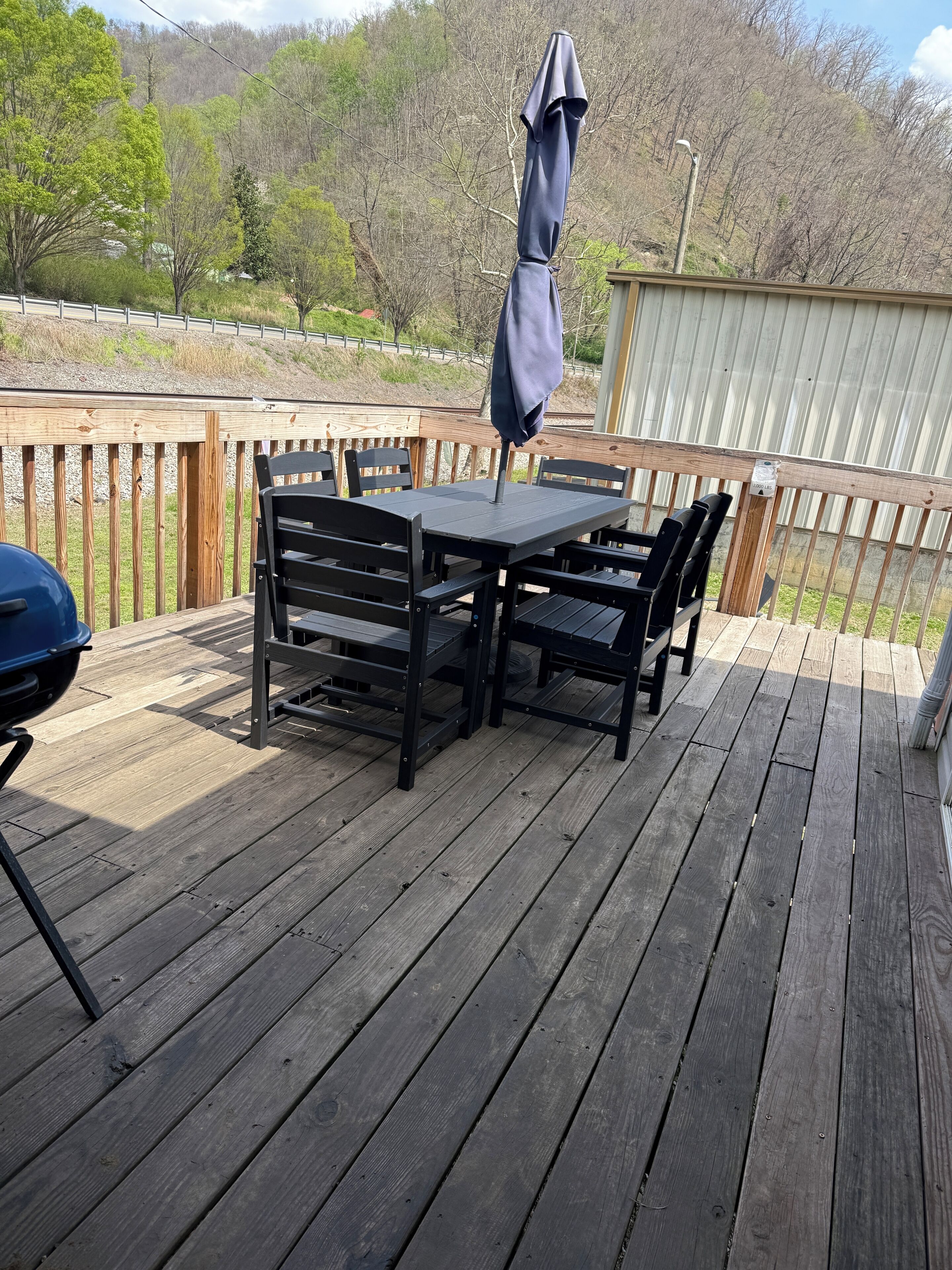 A wooden deck with a table and chairs, a barbecue grill, and a covered umbrella.