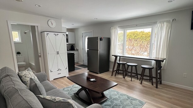 Ein modernes Wohnzimmer mit einem grauen Sofa, einem Holztisch und einem Essbereich mit Tisch und Hockern.