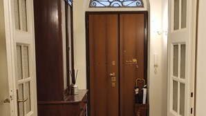 A hallway with a wooden cabinet, a door with a glass window, and a tiled floor. - MAISON '900 ANCIENT CHARMING APT IN ROME (Roma)