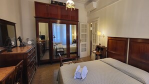 A hotel room with a large bed, wooden headboard, a desk with a lamp, a wardrobe, and a mirror. - MAISON '900 ANCIENT CHARMING APT IN ROME (Roma)
