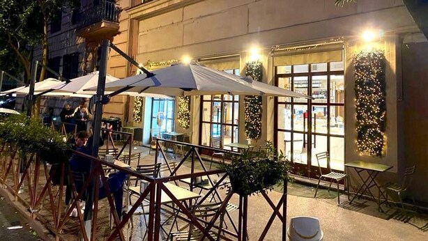 An outdoor cafe with tables and umbrellas, a building with large windows, and a tree in the foreground. - MAISON '900 ANCIENT CHARMING APT IN ROME (Roma)