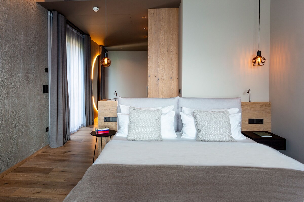 A modern hotel room with a large bed, wooden headboard, and a bedside table with a lamp.