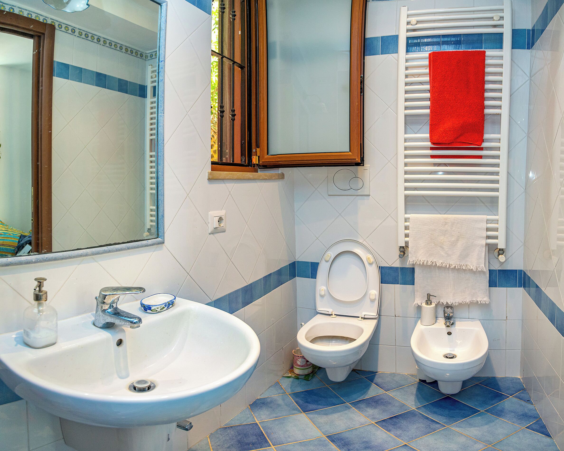 Une salle de bain avec un lavabo, deux toilettes et un porte-serviettes sur lequel est posée une serviette rouge.