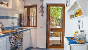 A kitchen with a blue tiled floor, white cabinets, a wooden door, and a small fish tank on the right. - Olivegrove Holiday House (Massalubrense)