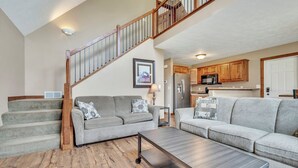 A living room with a staircase, two sofas, a coffee table, and a kitchen area.