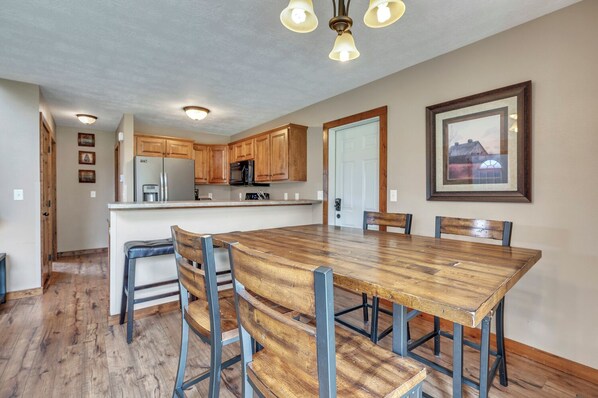 A dining area with a wooden table and chairs, a kitchen with wooden cabinets, and a framed picture on the wall.
