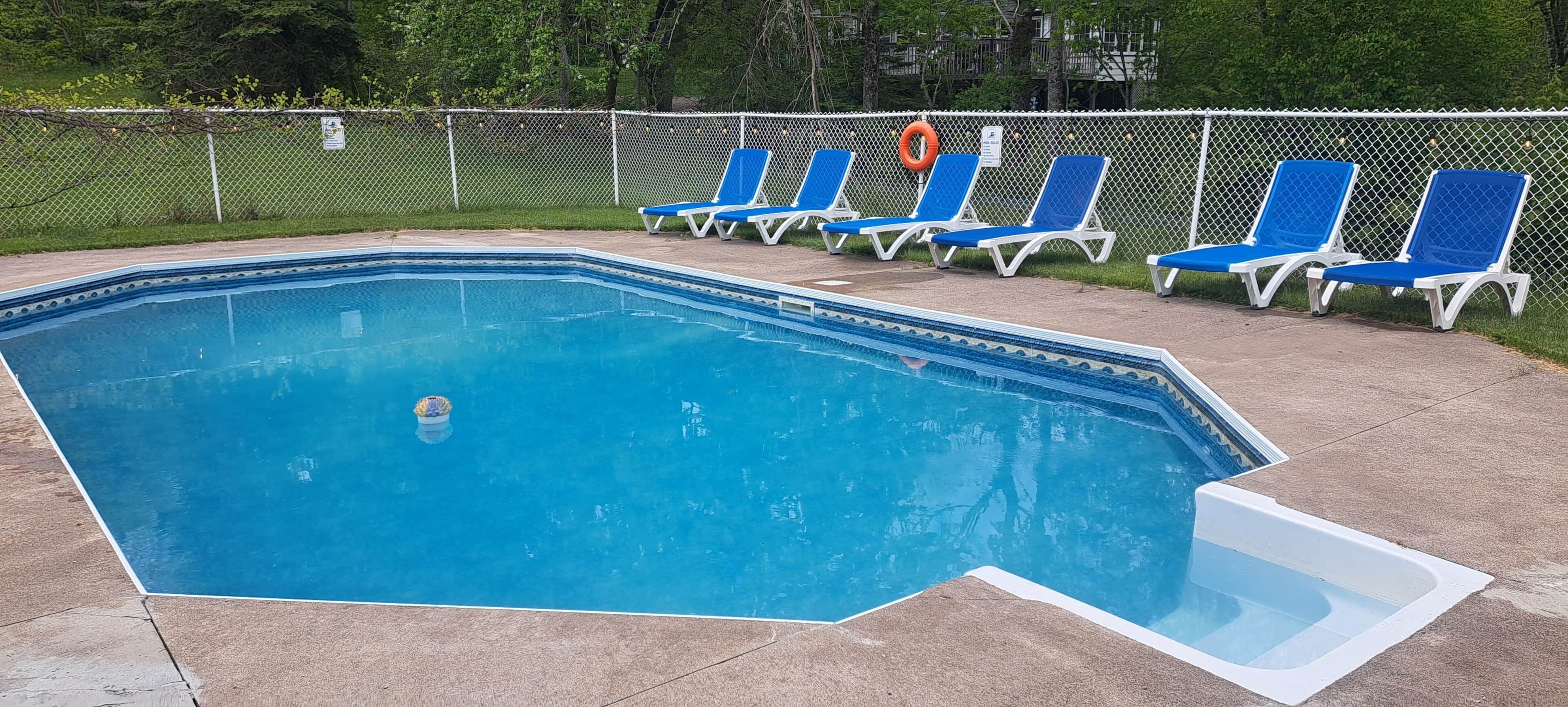 Una piscina con borde de azulejos, rodeada por una valla y sillas de descanso azules.