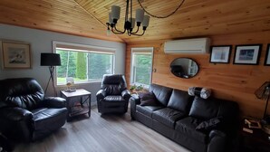 A cozy living room with a wooden ceiling, leather sofas, a small table, and a TV. - Lochaber Lake View Cottage (Antigonish County)