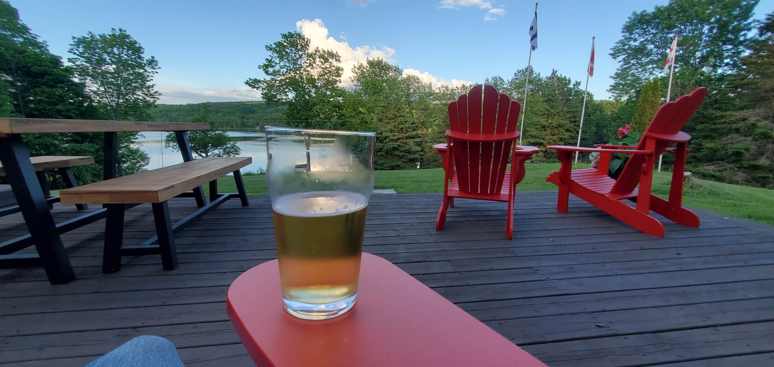 Un pontile in legno con un bicchiere di birra, poltrone Adirondack rosse e un tavolo da picnic.