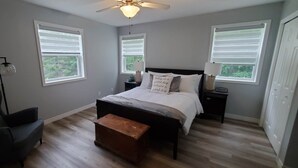 A bedroom with a bed, two bedside tables, a chair, a bench, and a ceiling fan. - Lochaber Lake View Cottage (Antigonish County)