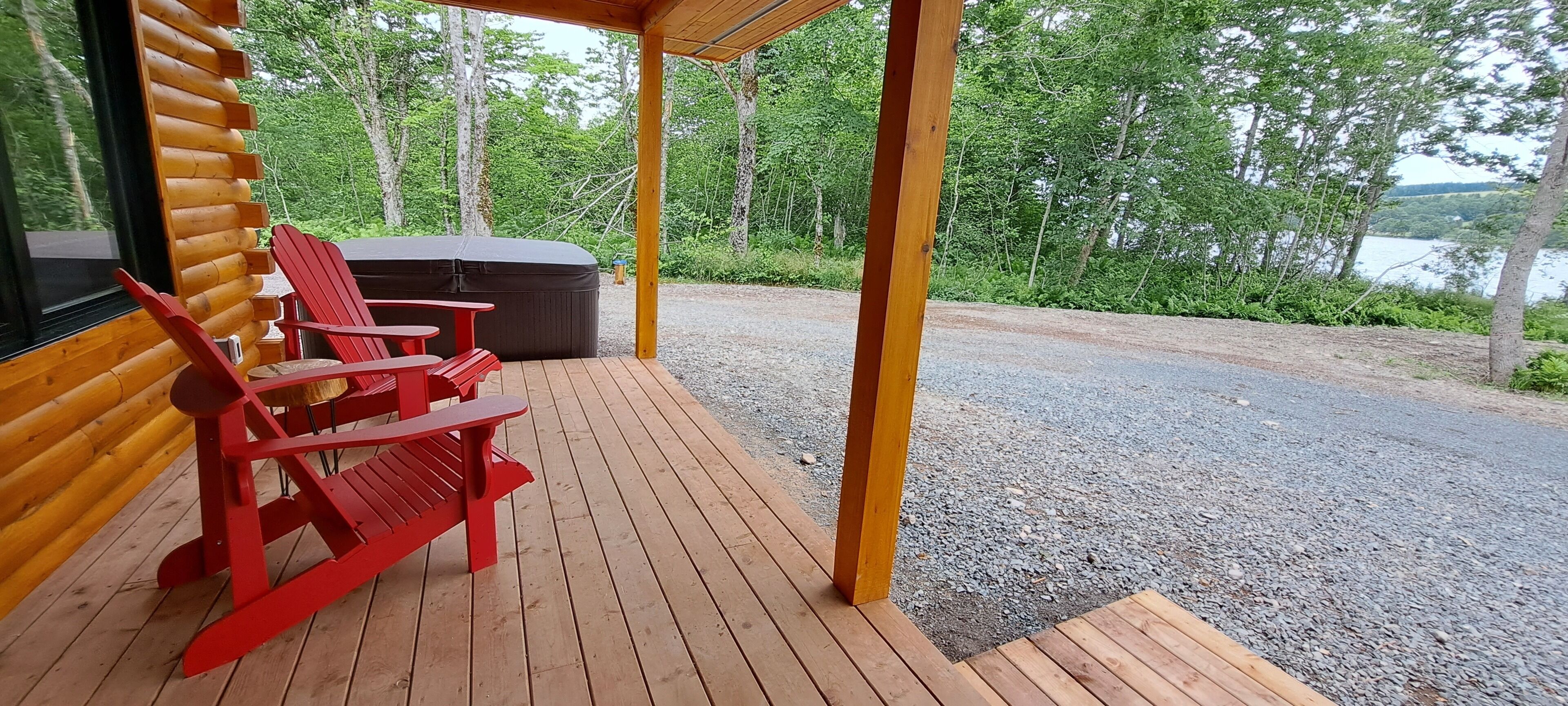 Een houten terras met rode Adirondack-stoelen en een jacuzzi.