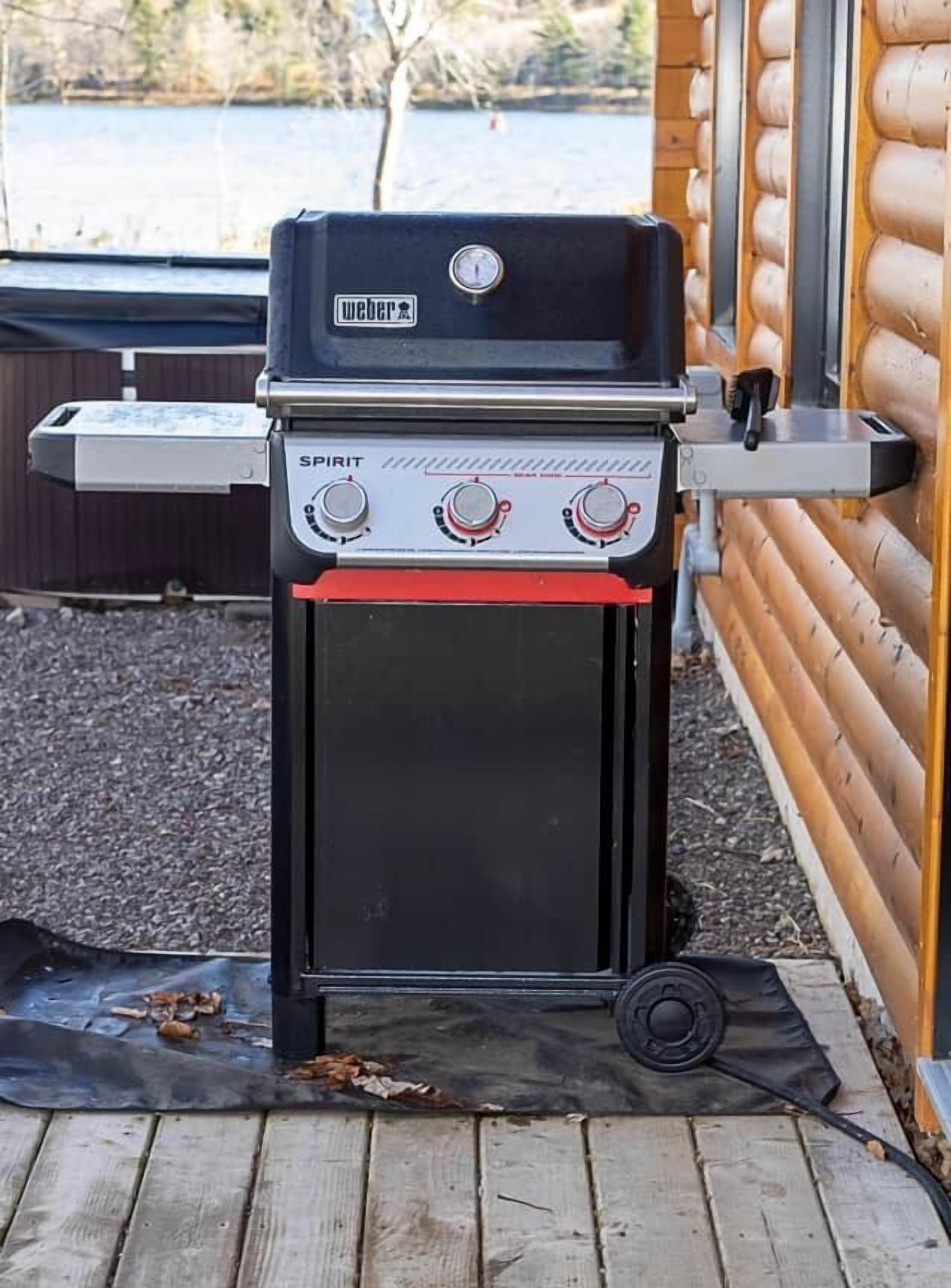 A Weber Spirit portable grill with three control knobs and a digital display, placed on a wooden deck.