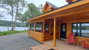 Une cabane en bois avec un porche, de grandes fenêtres et une vue sur un lac.
