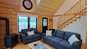 Un intérieur de chalet chaleureux avec deux canapés, un escalier en bois et un poêle à bois noir.