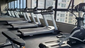 Ett gym med löpband och annan träningsutrustning, stora fönster och utsikt över byggnaderna utanför.