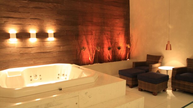 A modern bathroom with a large bathtub, wooden wall paneling, and a seating area with ottomans and a table. - Apple Motel - Adults Only (São Paulo)
