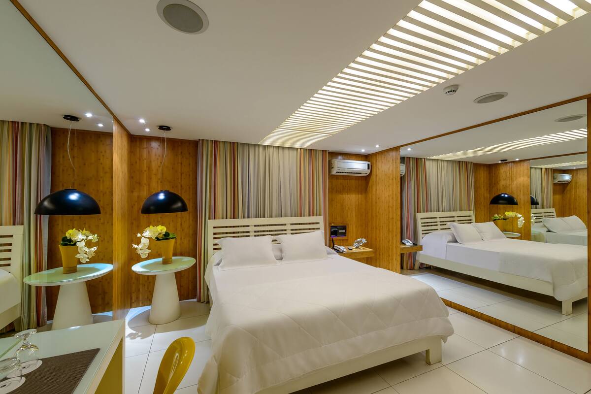 Una habitación de hotel moderna con una cama grande, dos mesitas de noche, un escritorio con una silla y un espejo.