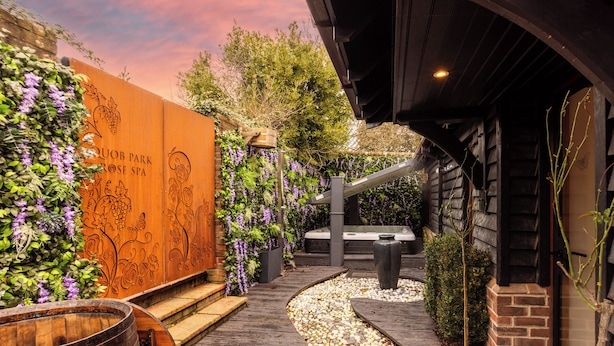 Een houten pad dat leidt naar een wellnessruimte met een pergola en een houten vat.