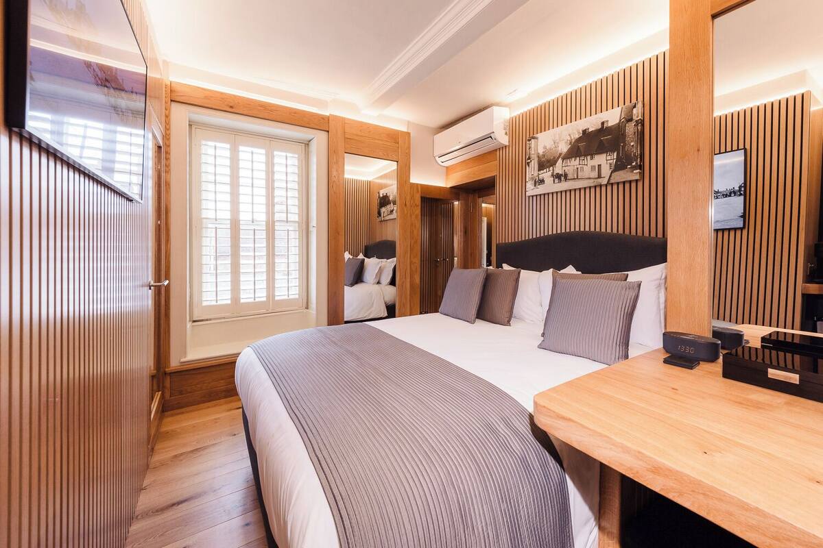 Een moderne slaapkamer met een groot bed, houten lambrisering, een nachtkastje en een wandairconditioner.